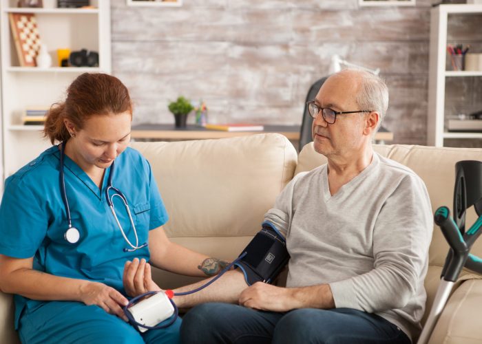 Female doctor in nursing home checking old man blood pressure.